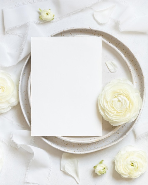 Wedding table setting with card near cream roses and white silk ribbons top view mockup