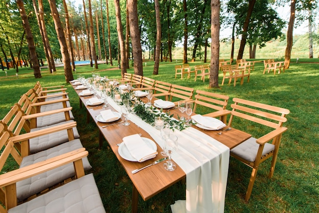 Wedding table with rustic decoration in the forest. Plates, and green branch with candles on the table. Green decoration.