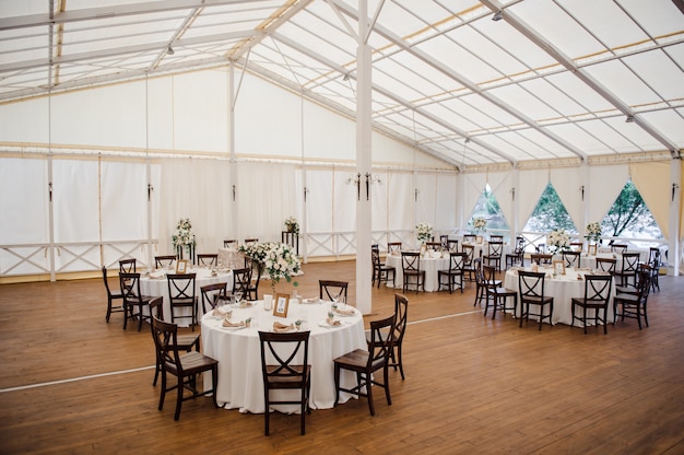 Photo wedding in a tent. decoration of the hall. white tablecloths, beautiful decor and dishes.