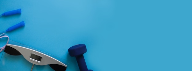 weigh scales skipping rope and dumbbells isolated on a blue background