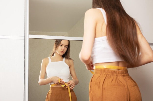 Weight loss A girl in front of a mirror with a measuring tape looks at figure