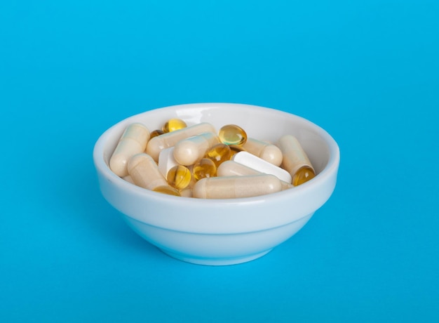 Weight Loss Pills in White Bowl Diet Supplements Capsules Obesity Lose Tablets Color Drugs Pile Weight Loss Pills on Blue Background with Copy Space for Text