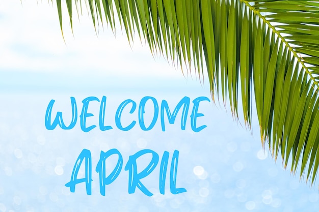 Welcome april message written in elegant font on the background with palm leaf and blue sea holiday ...