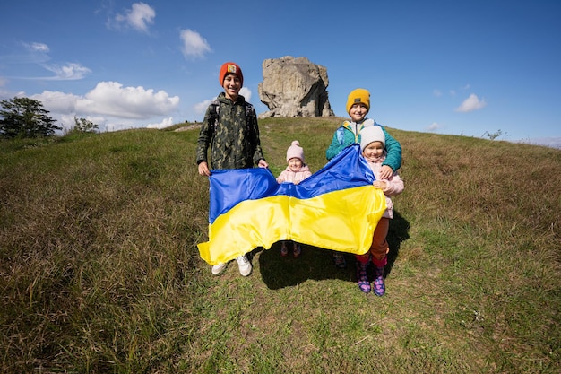 Welcome to Ukraine Four children hold ukrainian flag near big stone in hill Pidkamin