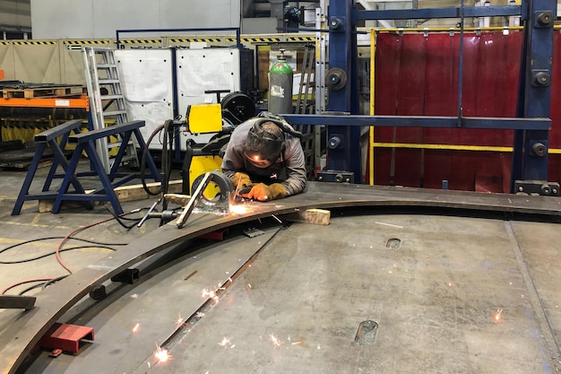 A welder in a mask welds large parts in a factory