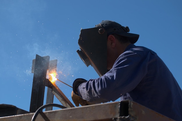 Welder welding a metal structure outdoors with occupational safety measures and personal safety equipment