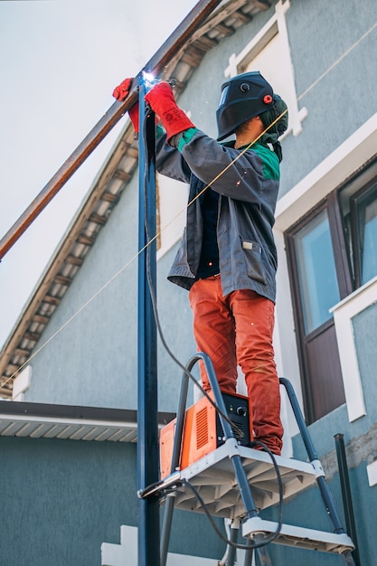 A welder welds a metal pole with electric welding, holds an electrode in his hands