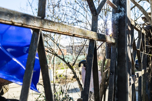 Welding of door hinge on gate of fence outdoors