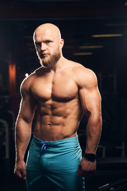 Well-built male athlete wearing shorts while standing at the gym and looking at the camera