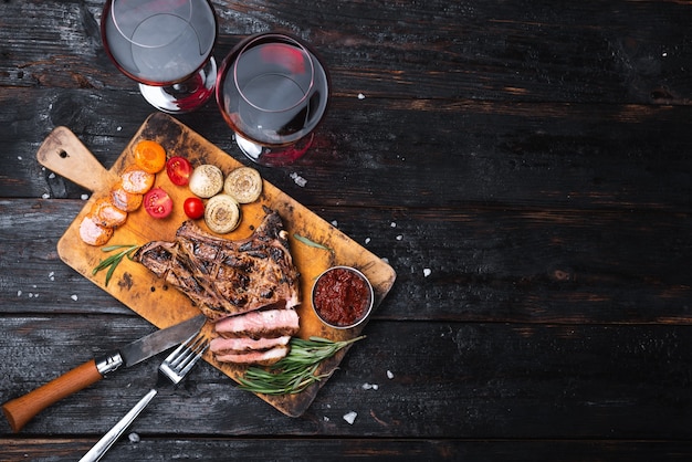 Well-done pork steak on a cutting board. Two glasses of dry red wine. Dinner for two place for text