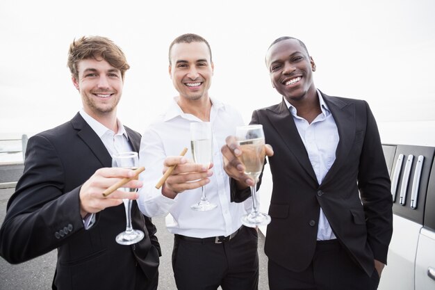 Well dressed men drinking champagne next to a limousine