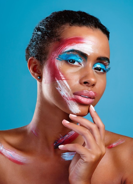 Wellcolour me intrigued Studio portrait of a beautiful young woman covered in face paint posing against a blue background