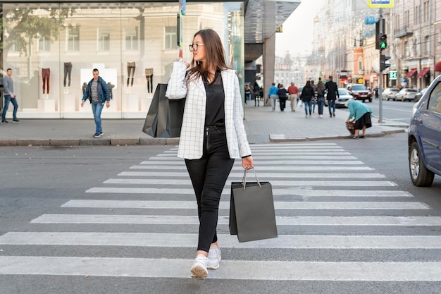 Welldressed young woman holds black paper bag with space to copy text or design Girl crosses road at pedestrian crossing