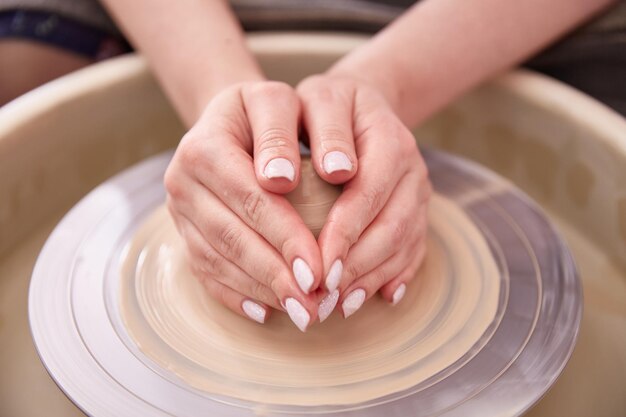 Wellgroomed female hands sculpt a cup of clay behind a potters wheel