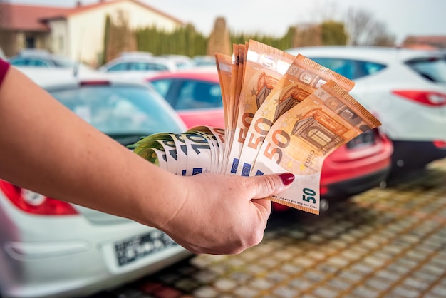 Wellgroomed female hands with manicure holding a round sum of euro banknotes in a car showroom