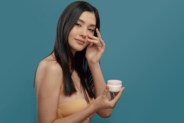 Wellgroomed girl holds round white cream jar with pink lid