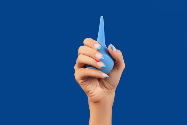 Wellgroomed womans hand holding enema on blue background