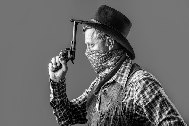 West, guns. Portrait of a cowboy. American bandit in mask, western man with hat. Portrait of cowboy in hat. Portrait of man wearing cowboy hat, gun. Portrait of a cowboy. Black and white.