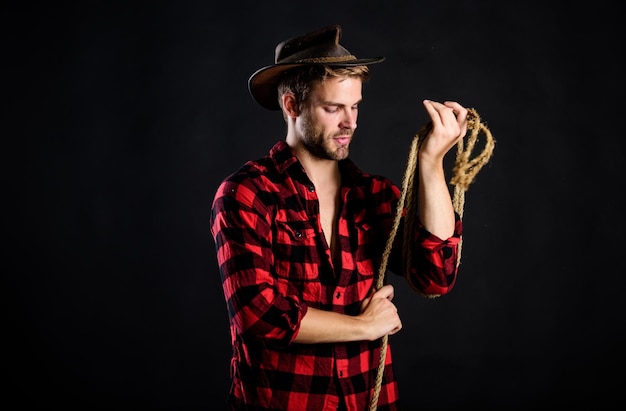 Western life Man unshaven cowboy black background Man wearing hat hold rope Lasso tool of American cowboy Lasso is used in rodeos as part of competitive events Lasso can be tied or wrapped