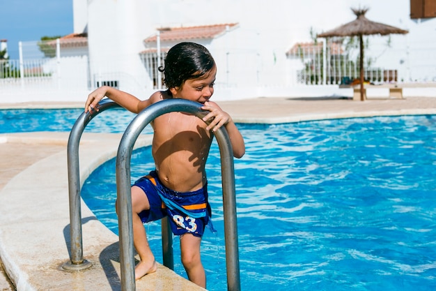 Wet boy just out of the pool, looks into the water and smiles with amusement