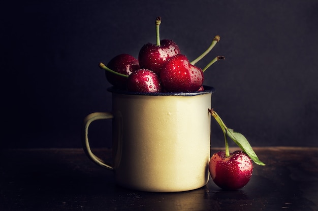 Wet cherries in a metal mug on a dark background