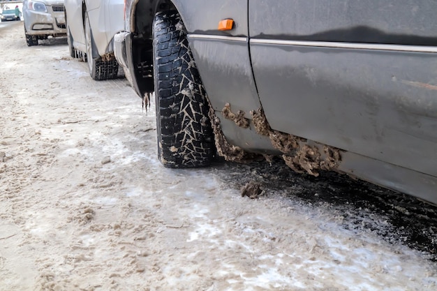 Wet dirty snow stuck to the car Mud covered salty gray car closeup