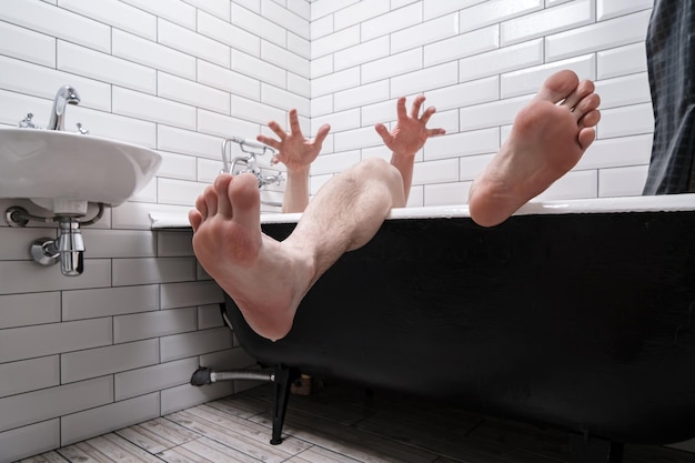 Wet male legs and hands with spread fingers are visible from the castiron bathtub in bathroom