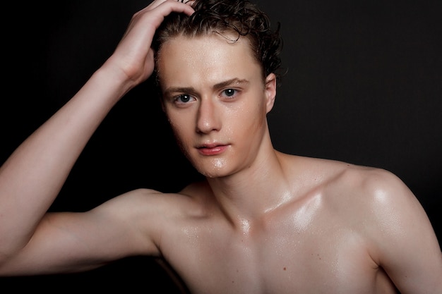 Wet young man with black hair on a black background