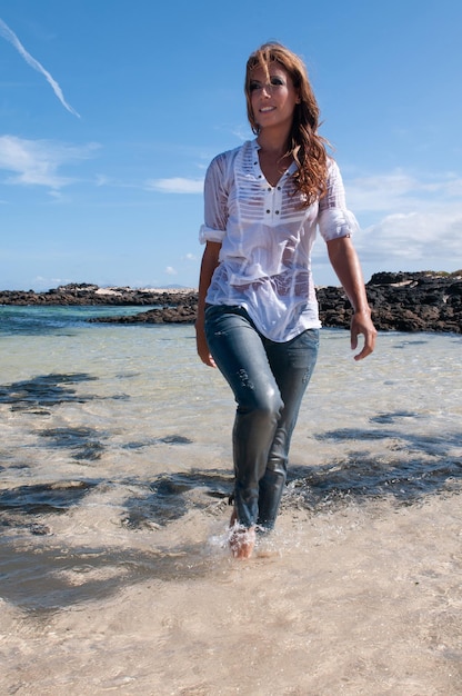 Wet young woman in clothes on the seashore in spring or summer under a blue sky