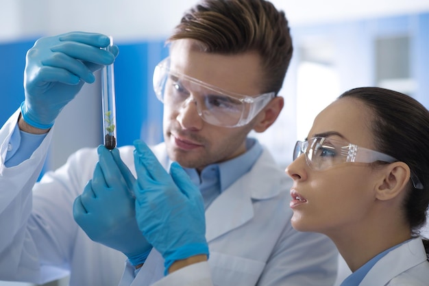 What is ist Two smart interested pleasant scientists in a glasses and rubber gloves standing in the laboratory concentrating their attention on the test tube and overlooking it