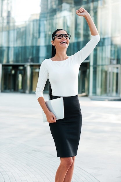 What a lucky day! Cheerful young businesswoman keeping arms raised and expressing positivity