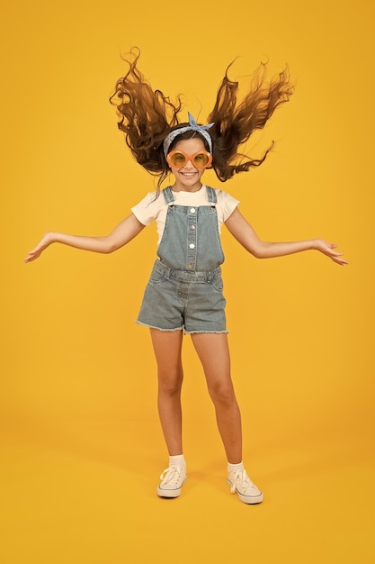 What a volume retro child long hair small girl vintage look sunglasses happy childhood joyful summer vacation haidresser salon concept spring kid fashion cheerful little girl yellow background