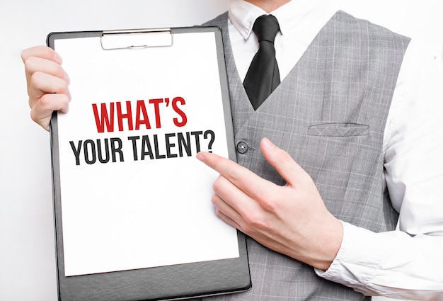 Whats Your Talent inscription on a notebook in the hands of a businessman on a gray background