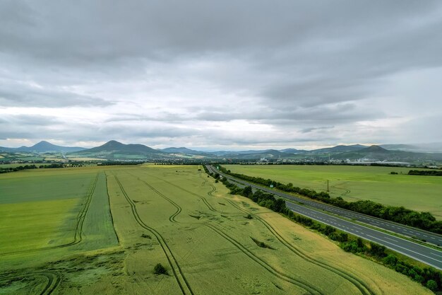 Wheat field near a flat road. View from above on a green field. Countryside. Near the field forest and mountains.