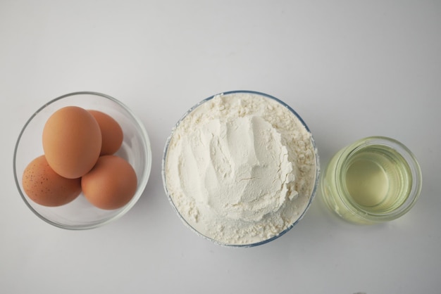 Wheat flour in a bowl eggs and oil on table