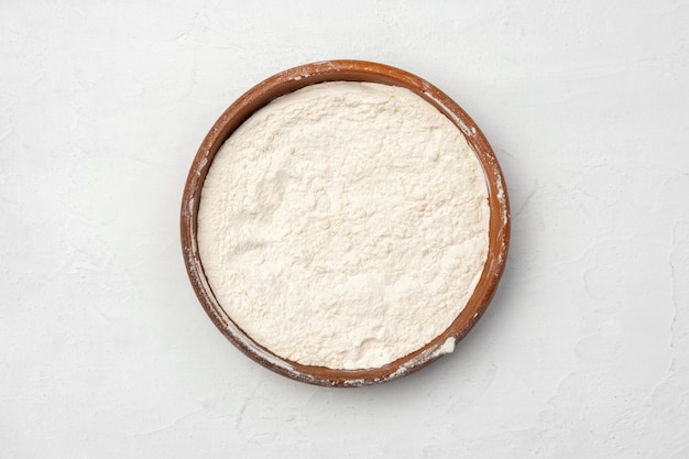 Wheat flour in ceramic bowl on white background top view