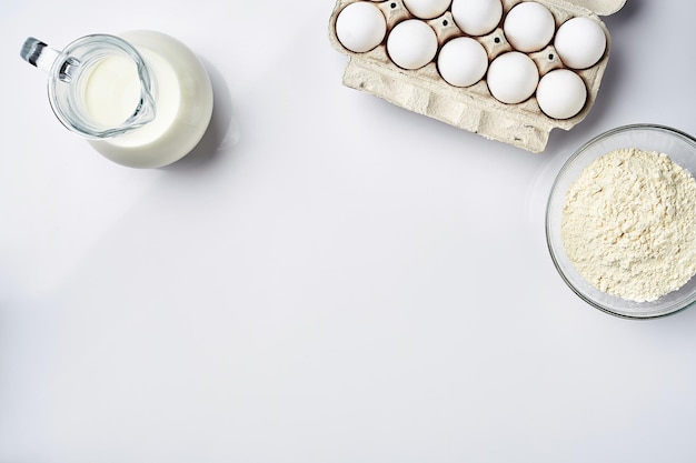 Wheat flour in the glass bowl cream in a glass jar chicken eggs ingredients for the dough top view