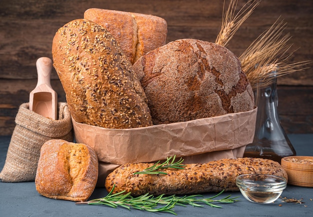 Wheat and rye bread of different types, butter and rosemary on a wooden background. Side view, close-up.