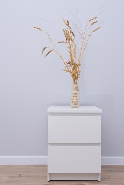 Wheat in a vase on a bedside table against a gray wall.