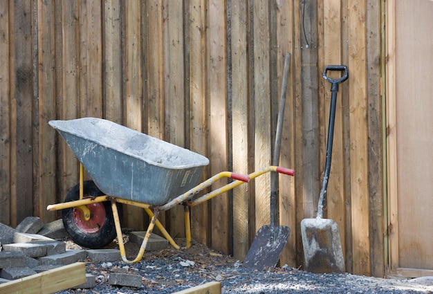 A wheelbarrow and spade placed amongst gravel and building material Construction site at a home in the backyard Equipment and tools used to build a house A shovel and other building equipment