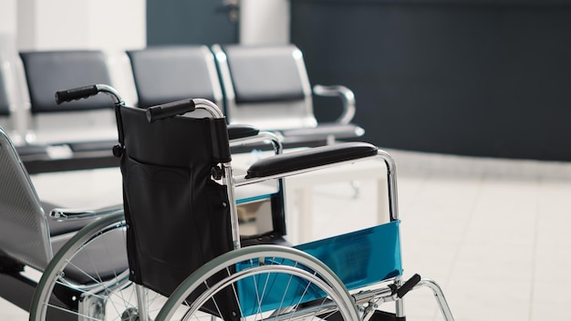 Wheelchair in empty waiting room used for physical recovery service on health care insurance, disability friendly clinic. Reception counter for registration with seats and medical forms.