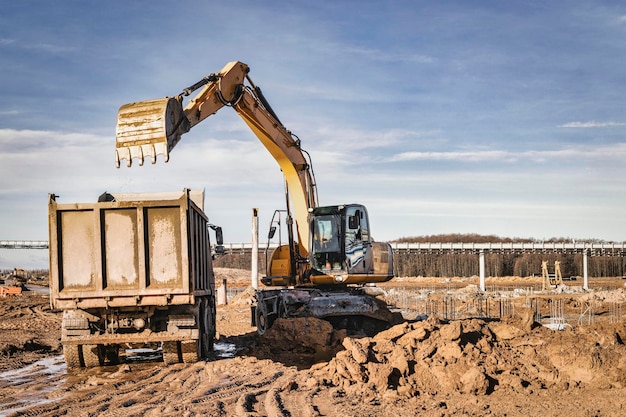 A wheeled excavator loads a dump truck with soil and sand The excavator digs the ground at the construction site Removal of soil from a construction site or quarry