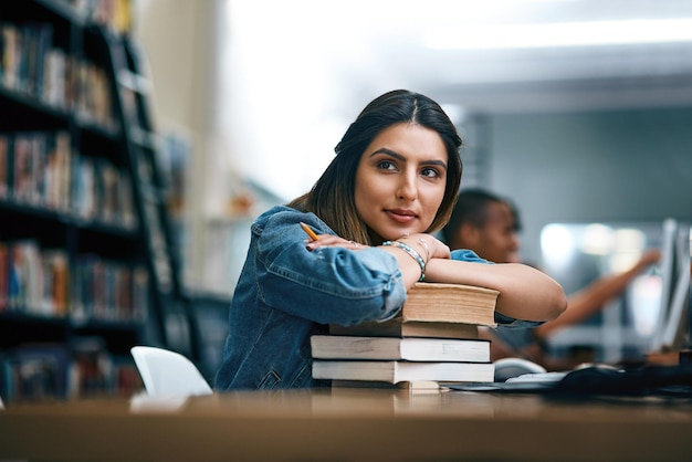 Where dreams are turned into reality Shot of a young woman resting on a pile of books in a college library and looking thoughtful