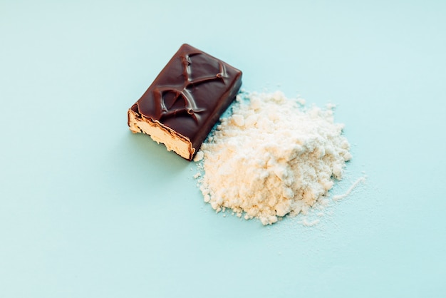 Whey protein powder and energy bar on blue wall.