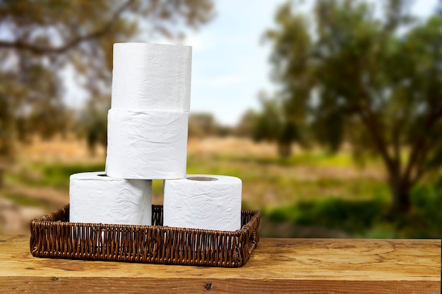 whicker basket with rolls of toilet paper on wooden board table with copy space and near blur olives