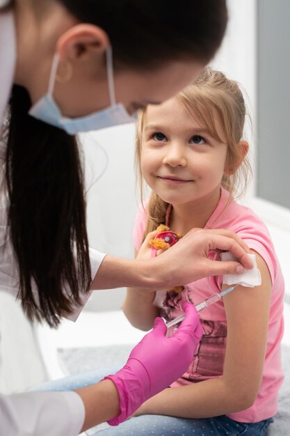 While receiving the vaccine the girl smiles gently and looks confidently into the nurses eyes The doctor stabs the child in the arm with a needle Preventive vaccine for young children