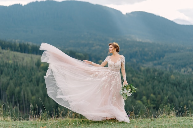 Whirling bride holding veil skirt of wedding dress at pine forest