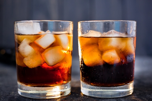 Whiskey or rum with cola and ice in glasses on a dark background