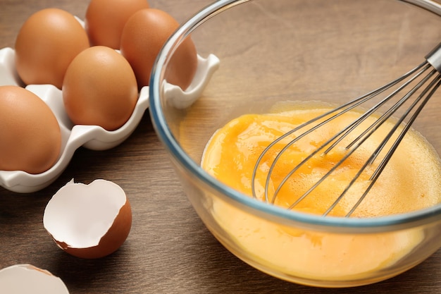 Whisking eggs in glass bowl on wooden table closeup