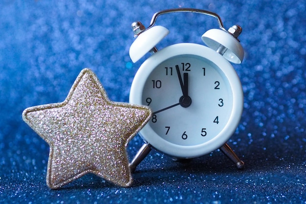 White alarm clock on a blue shiny background and a golden star.